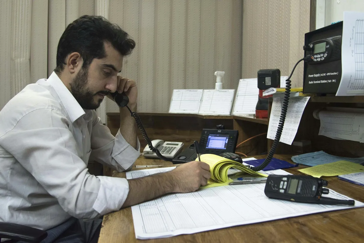 Receptionist on a desk phone writing caller details into a printed call log