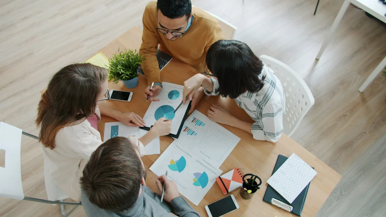Team comparing printed charts and options around a meeting table