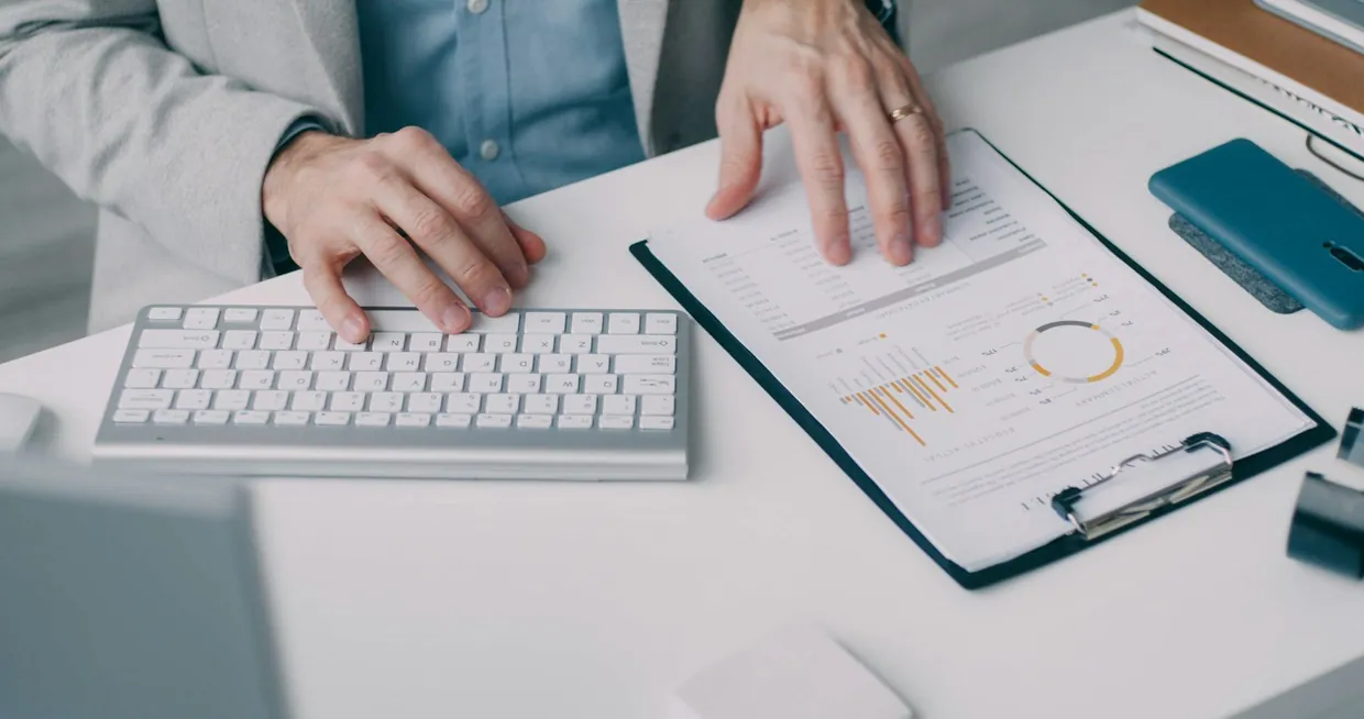 Typing beside a clipboard report of support charts while reviewing core KPIs