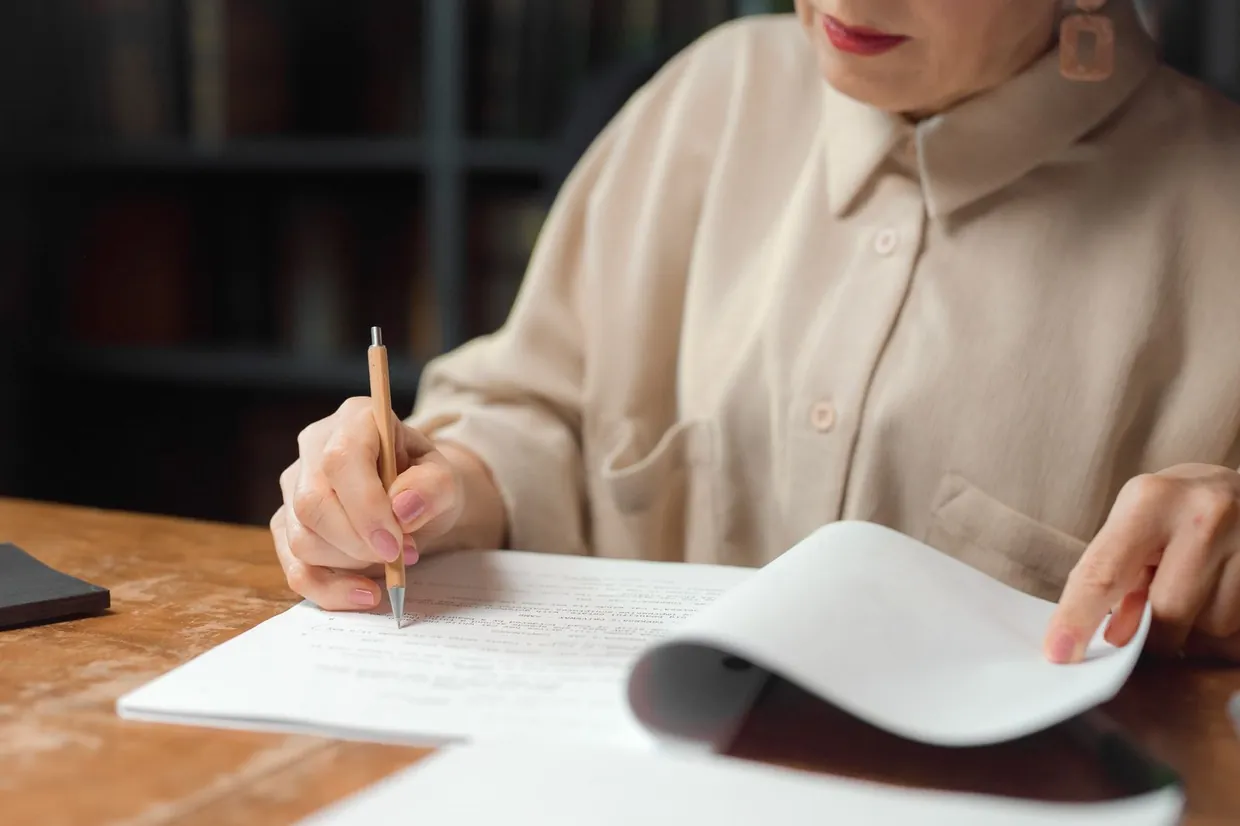 Woman marking up a printed document with a pencil at a wooden table while adapting a template