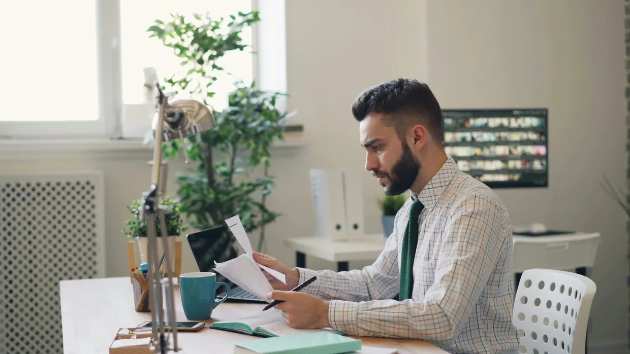 Executive assistant reviewing printed papers at a desk while preparing documents for a director
