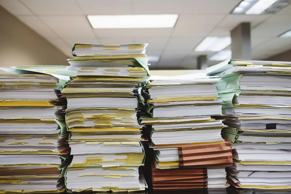 Tall stacks of paper files in an office, showing the workload an assistant has to absorb