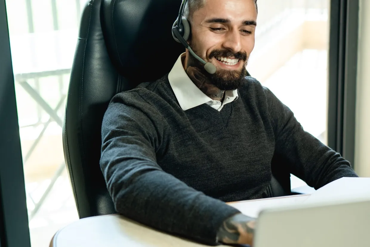 Customer support agent with a headset working at his laptop in a bright office