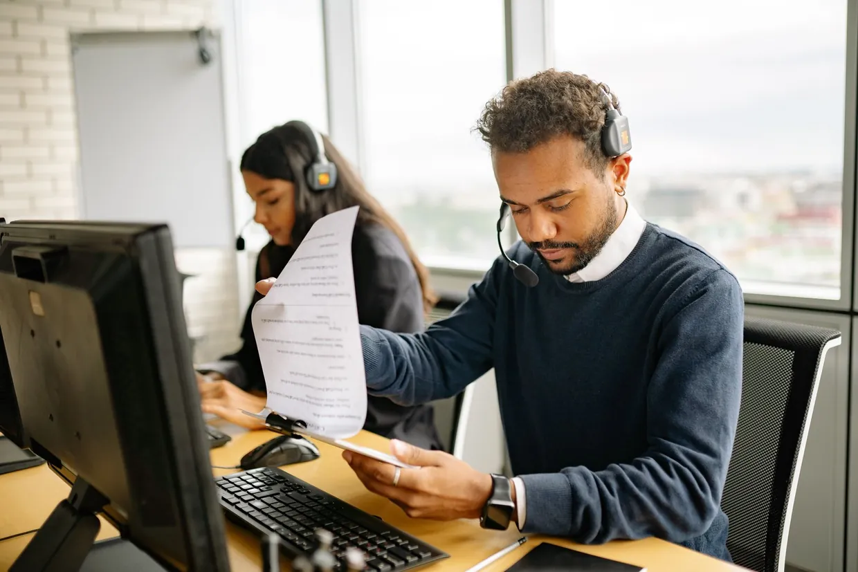 Agent with a headset reviewing a printed sheet at his desk while qualifying an inbound lead