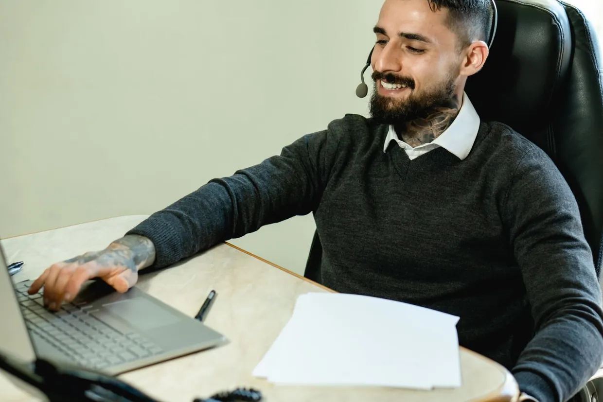 Caller on a headset working at a laptop with notes to hand during a cold calling session