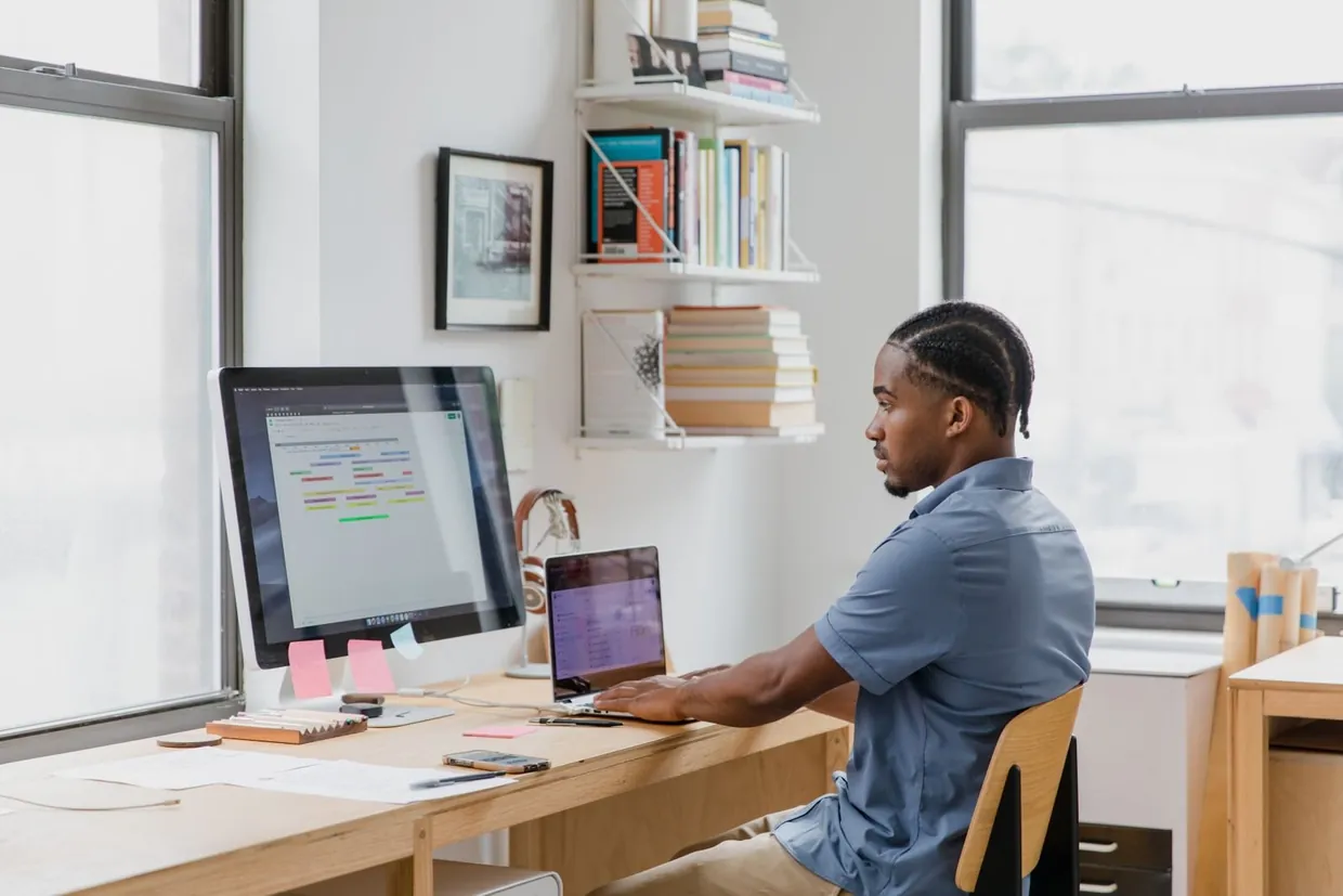 Man at a desk using a monitor and laptop to run lead generation tools such as a CRM and booking calendar