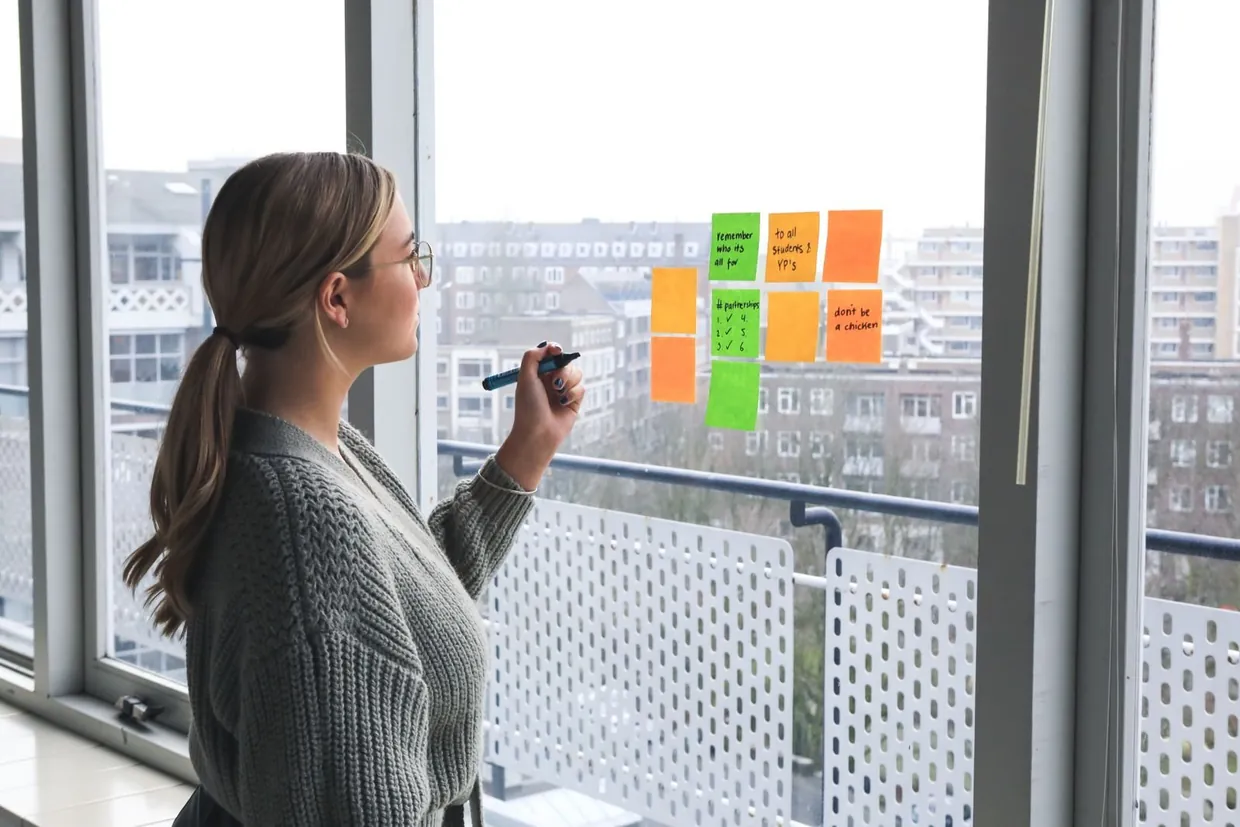 Woman sorting colour coded sticky notes on a window while planning lead and demand generation priorities