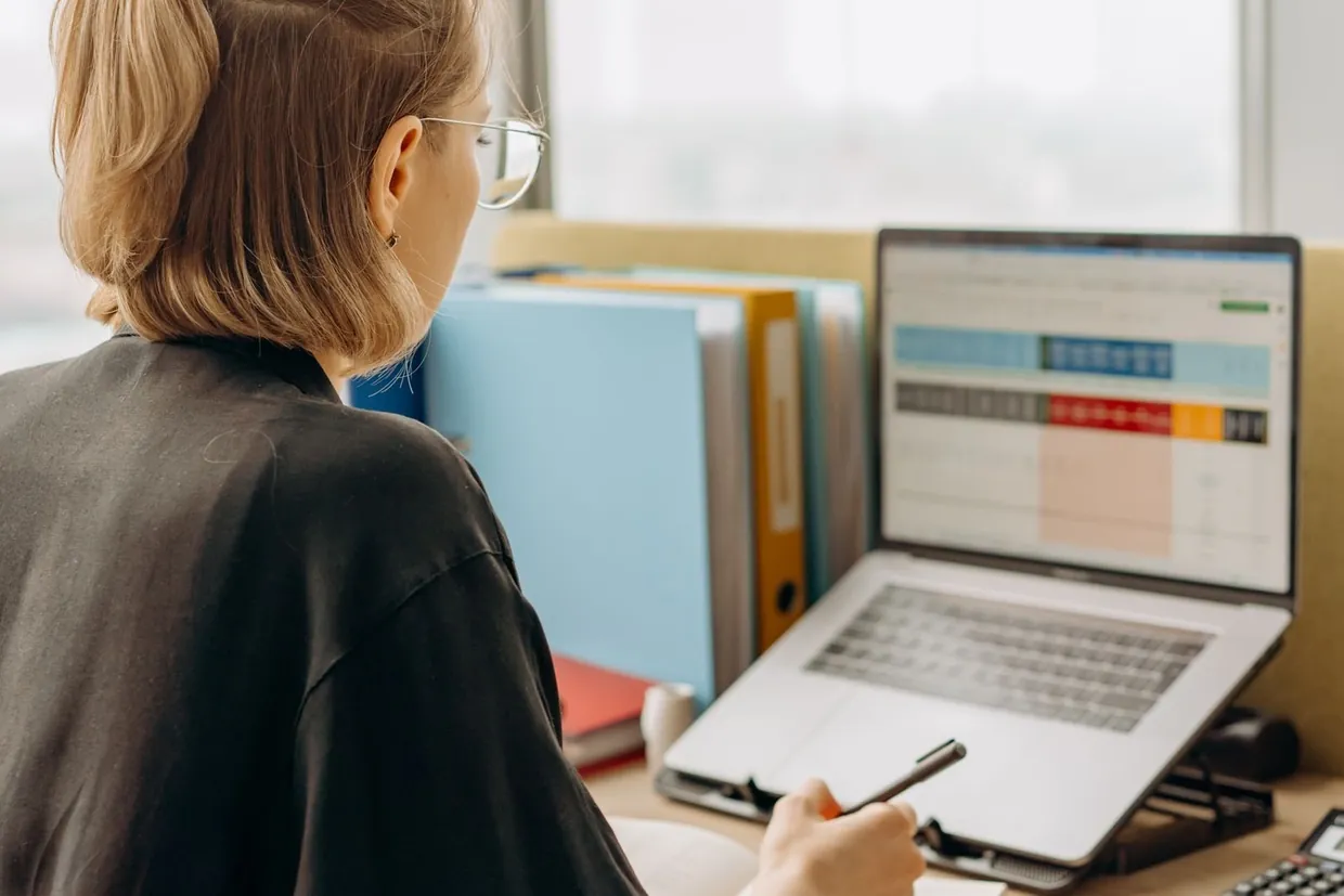 Woman building a lead list in a spreadsheet on her laptop, pen in hand and files beside her