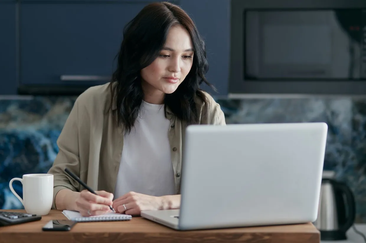 Woman logging LinkedIn acceptance and reply figures in a notepad while checking her laptop