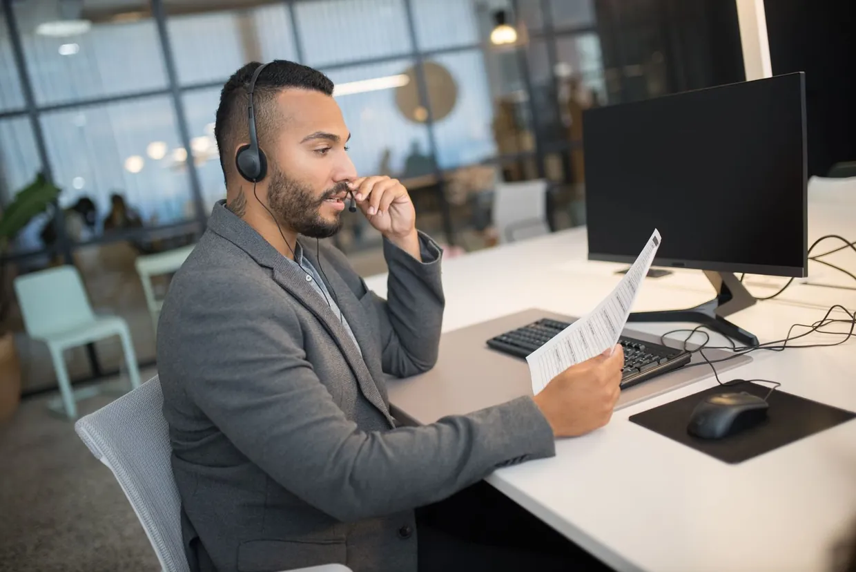 Receptionist on a headset holding a written note while taking a phone message to pass on