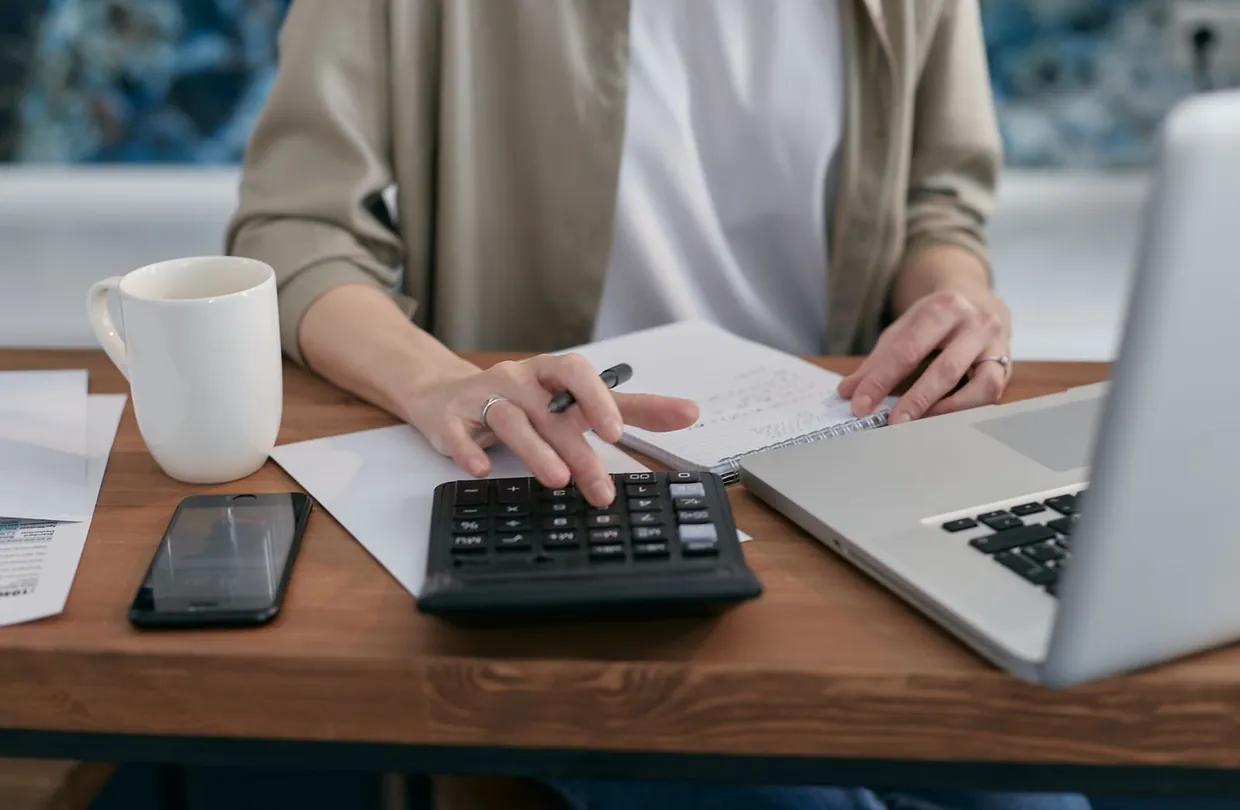 Working out time and cost of order processing steps with a calculator, notepad and laptop
