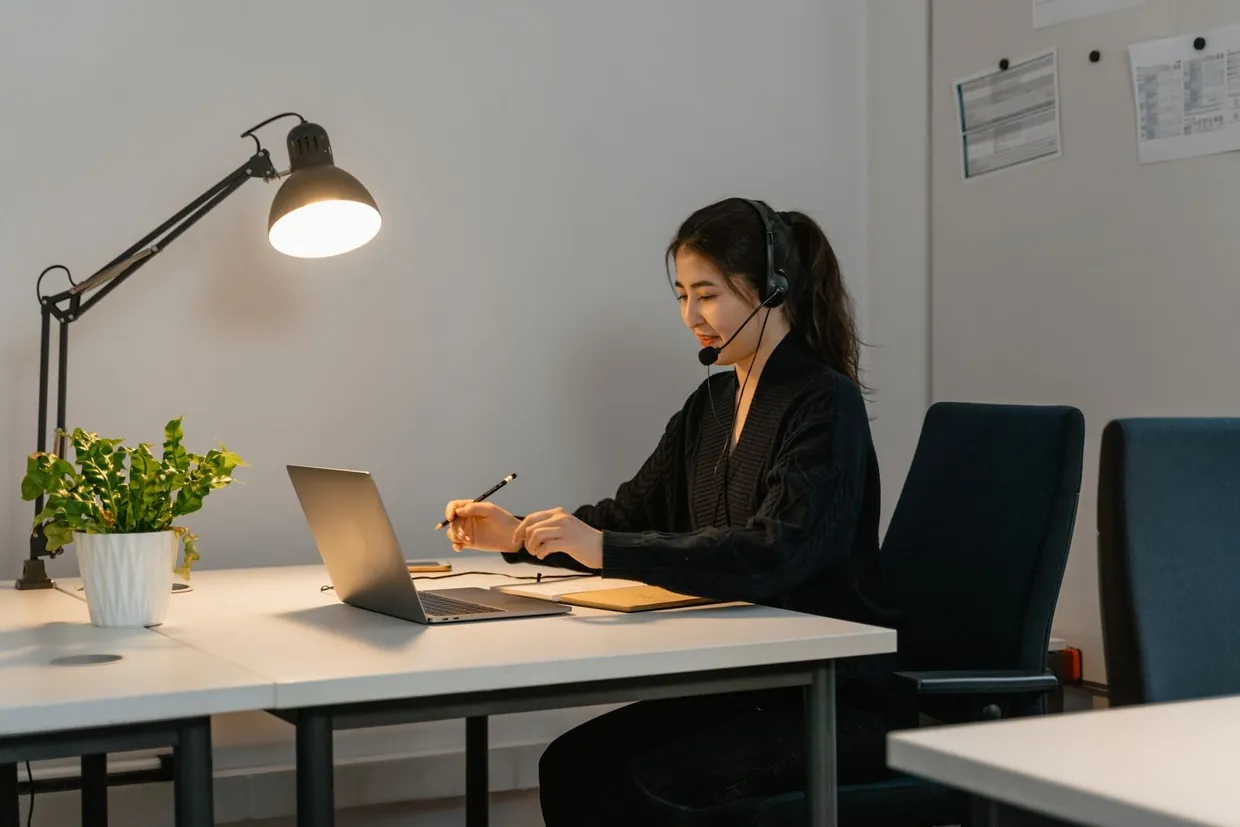 Customer service virtual assistant on a headset making notes at a laptop in a bright office