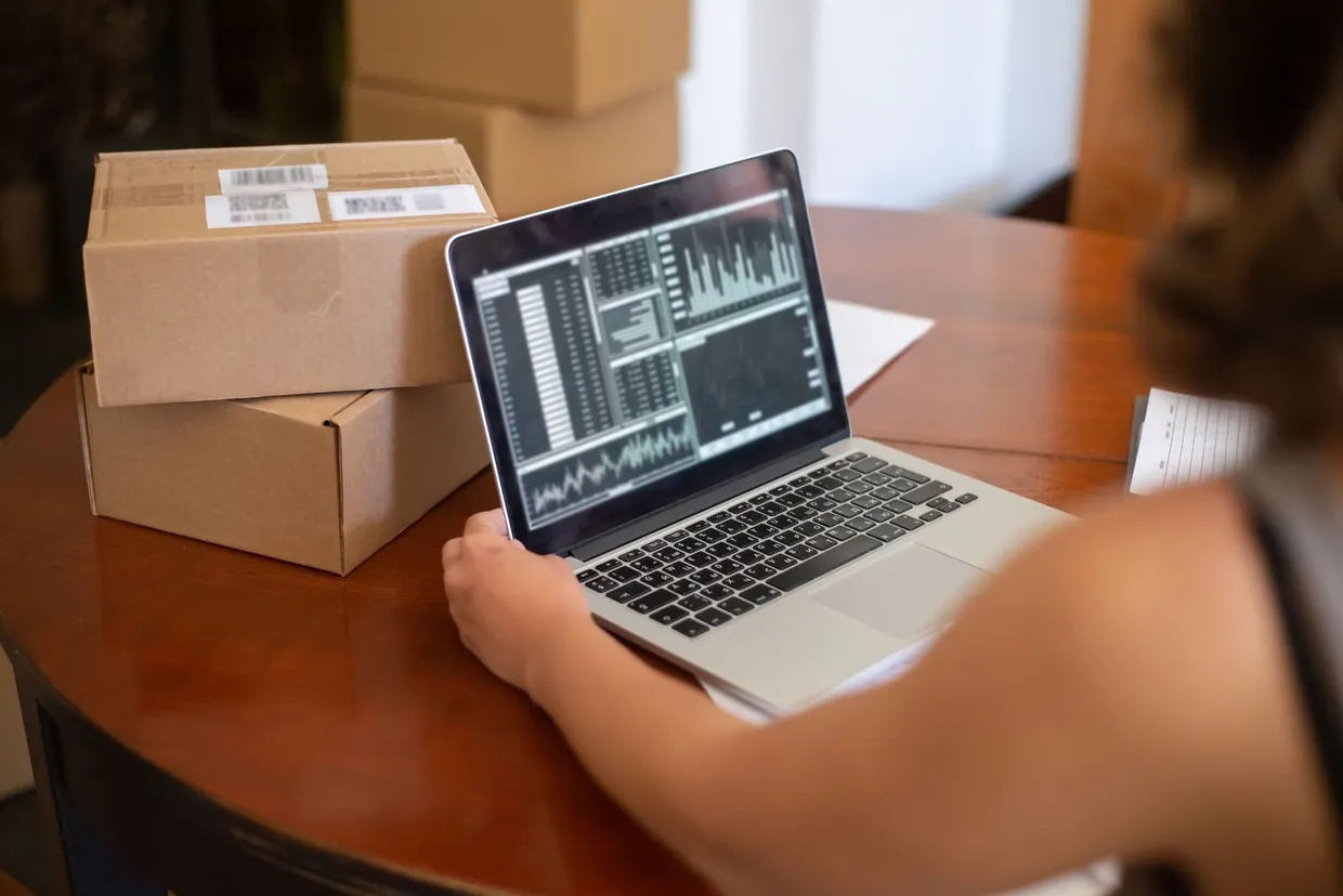Reviewing stock data on a laptop dashboard next to boxed stock to trigger automated reorders