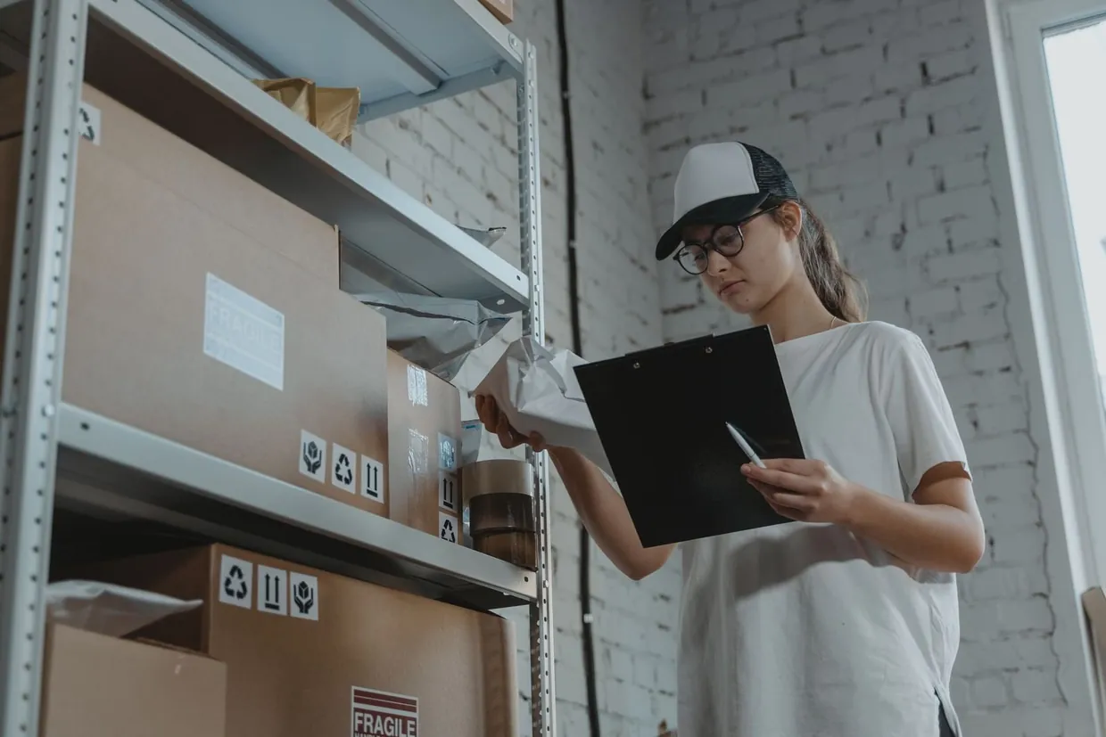Warehouse worker checking boxes on a stock shelf against a clipboard to work out reorder points