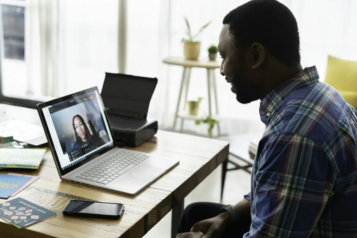 Small business owner on a video call with a virtual assistant provider, notes and phone at hand