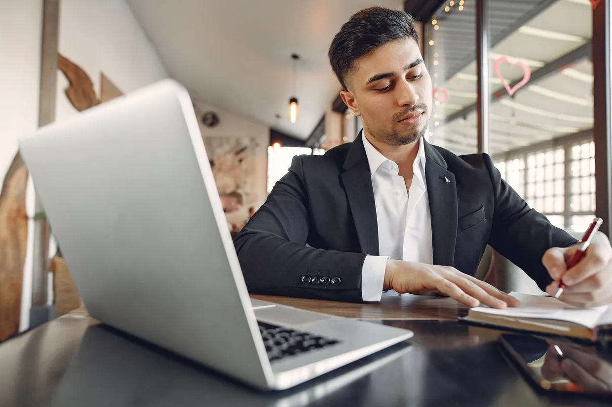 Drafting a virtual assistant job description, writing notes beside a laptop